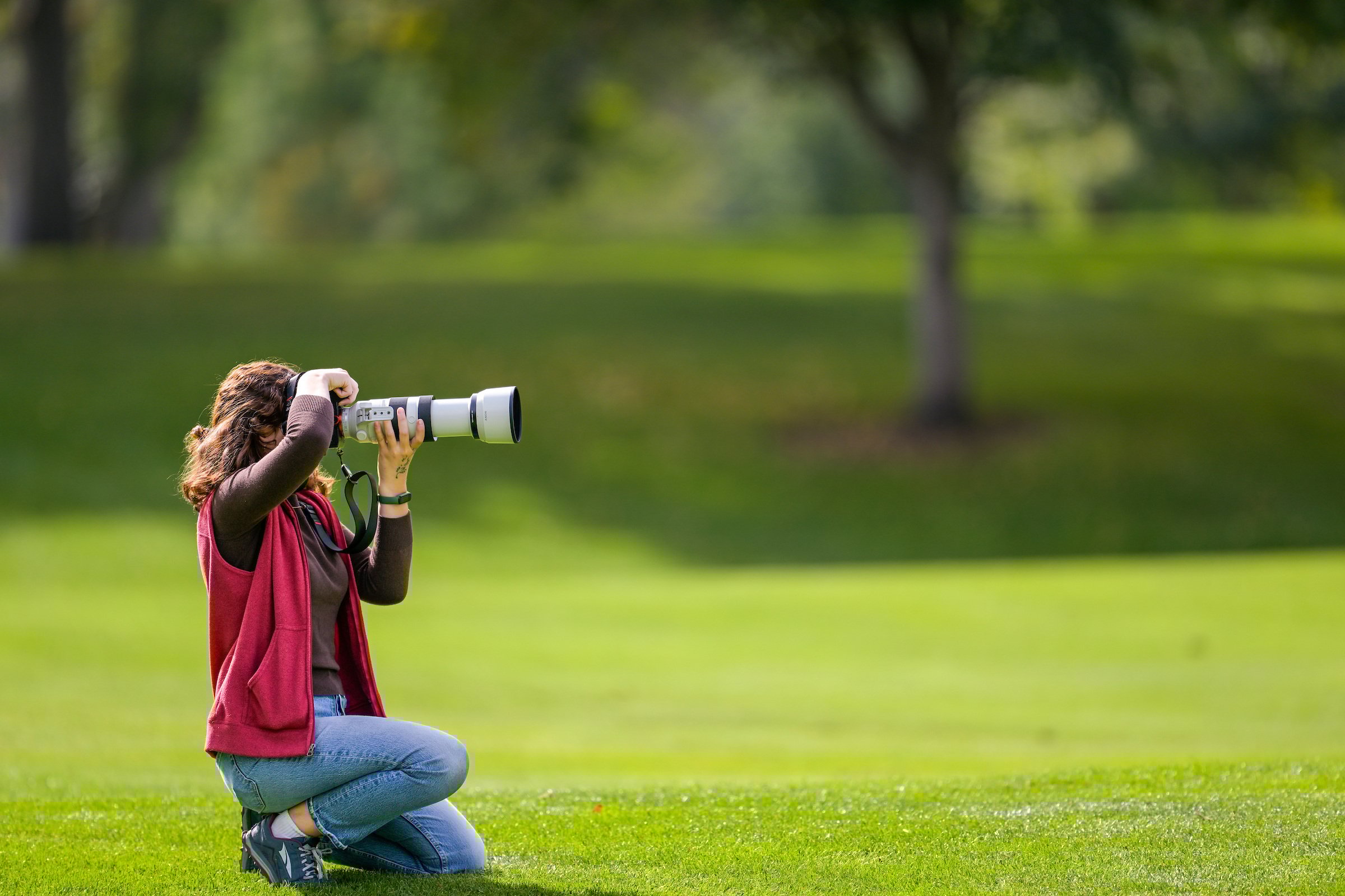 A female photographer kneels to take a photo during an event on UM's campus.