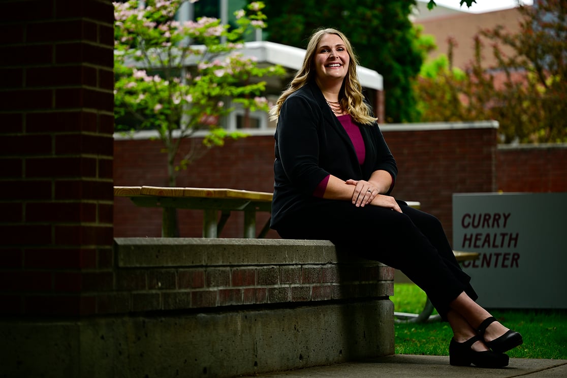 Jenna Musick sitting on a brick bench outside of Curry Health Center, posing for the camera