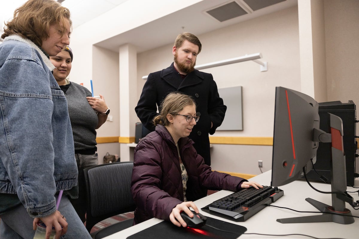 UM Students grouped around a computer monitor and workstation.