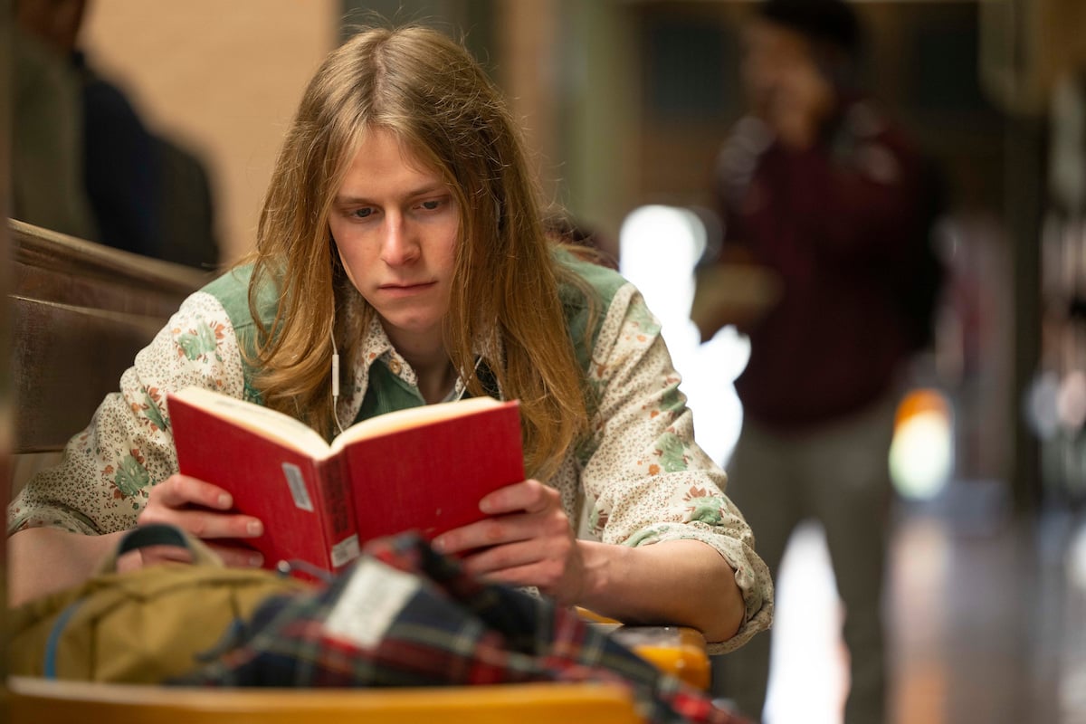 A UM student in a long sleeved shirt sitting and reading a hardback book with a red cover