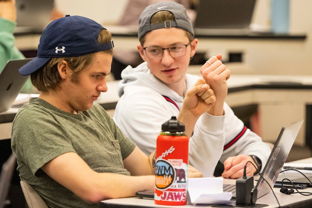 UM students sitting at a table and fist bumping while attending a Personal Finance course in the Gallagher Business Building at the University of Montana.
