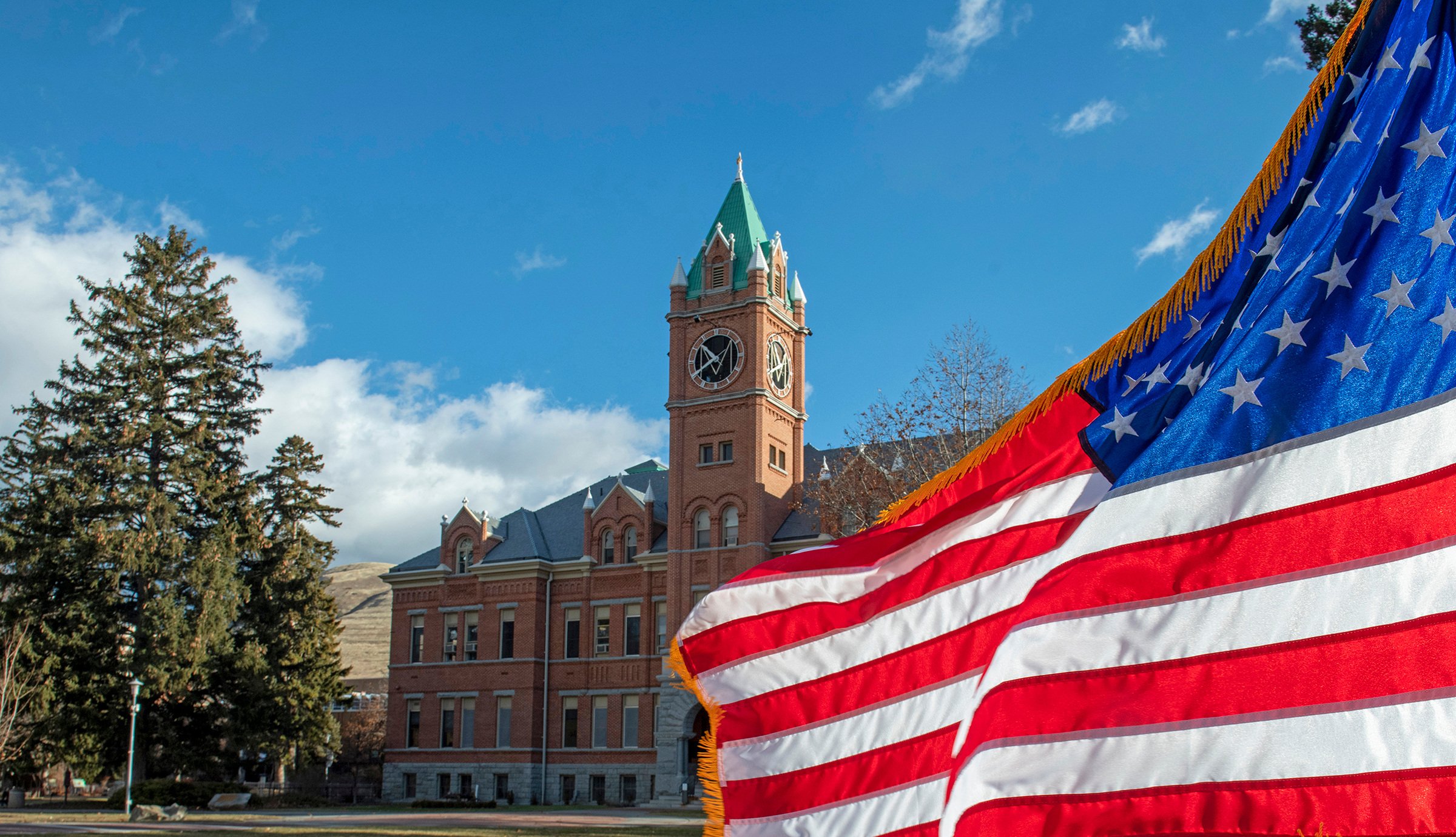 An American Flag flies in front of Main Hall on a sunny day on the University of Montana campus.